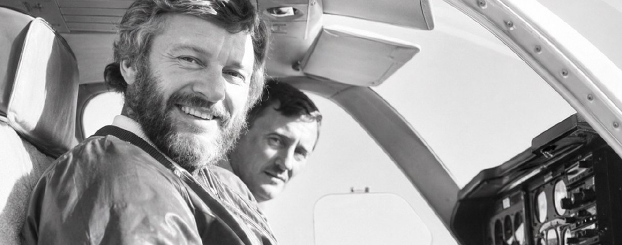 Two men seated in the cockpit of a light aircraft, black and white photograph